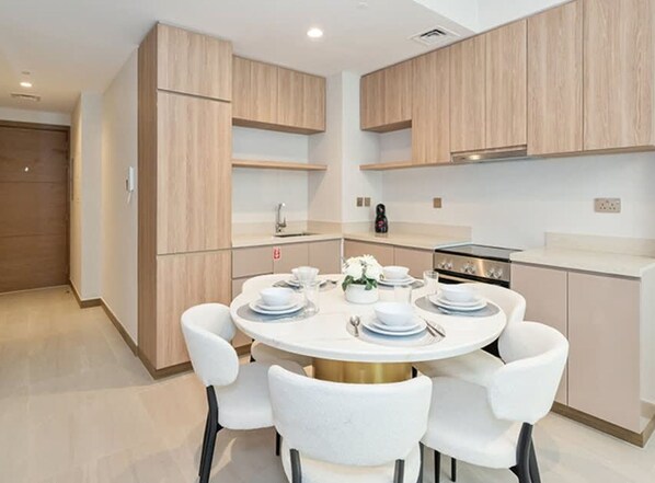 A modern kitchen with wooden cabinets, a round dining table with white chairs, and a built-in oven. - Stylish 2BR Fully Furnished Unit at Missoni (Dubai)