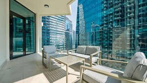 A modern balcony with a sofa, chairs, and a table, overlooking a cityscape with tall buildings. - Stylish 2BR Fully Furnished Unit at Missoni (Dubai)