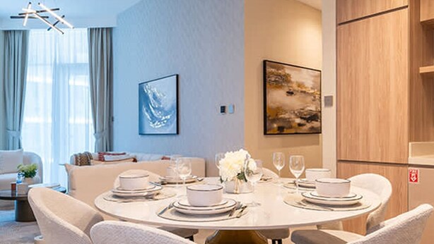 A modern dining area with a round table set for four, surrounded by white upholstered chairs. - 2-br Missoni Luxury With Stunning Lake View (Dubai)