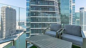 A high-rise building with a glass facade, a balcony with outdoor furniture, and a view of the cityscape. - 2-br Missoni Luxury With Stunning Lake View (Dubai)