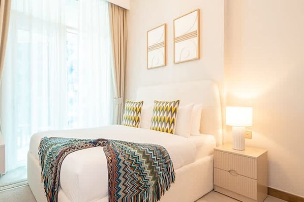 A hotel room with a large bed, a bedside table with a lamp, and two wall-mounted artworks. - Stylish Missoni 1BR Luxury Stay Ideal for 5 Guests (Dubai)
