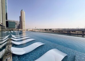 A rooftop infinity pool with white floating loungers, a view of a tall building, and a bridge in the background. - Stylish Missoni 1BR Luxury Stay Ideal for 5 Guests (Dubai)