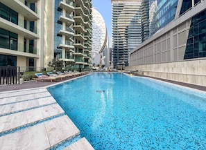 A swimming pool with lounge chairs, surrounded by modern high-rise buildings. - Stylish Missoni 1BR Luxury Stay Ideal for 5 Guests (Dubai)