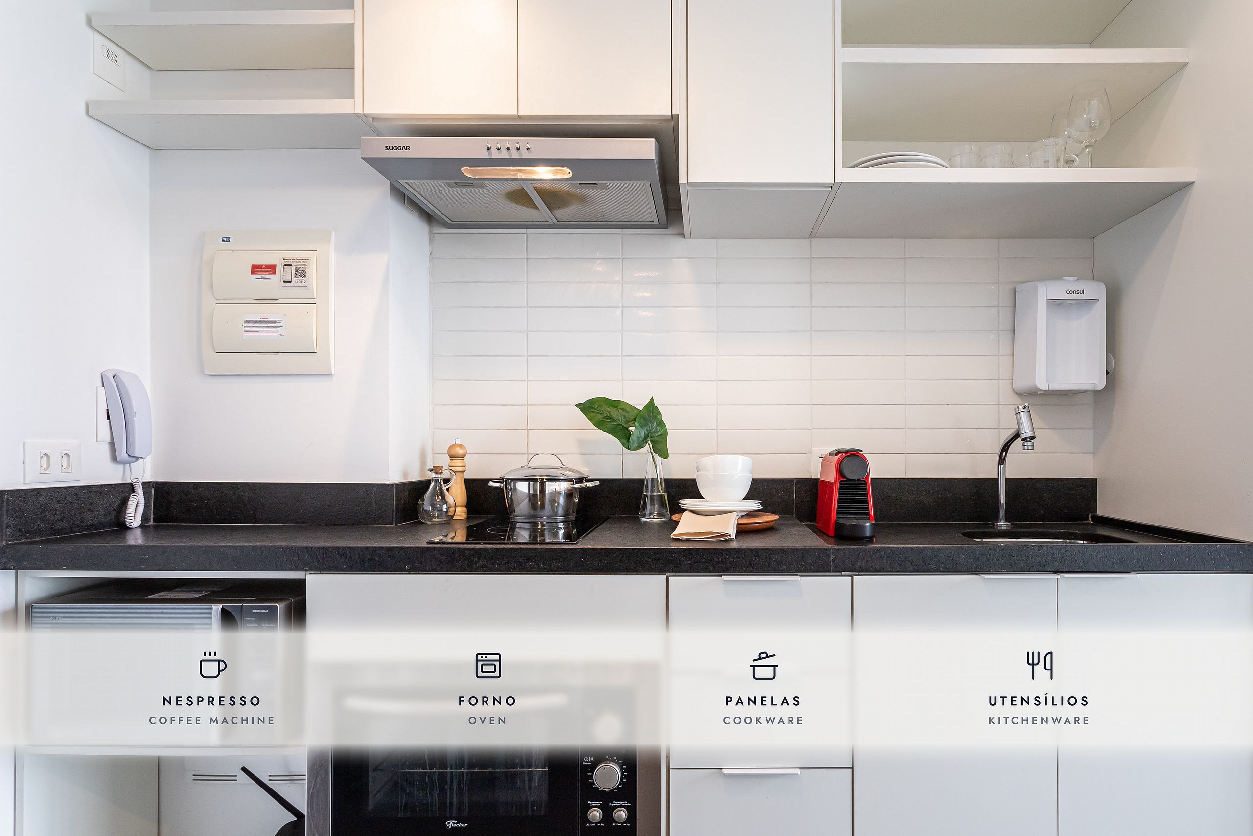 Una cucina moderna con mobili bianchi, un piano di lavoro nero e diversi elettrodomestici, tra cui una macchina da caffè, forno, pentole e utensili.