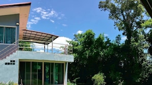 Una casa moderna de dos pisos con fachada de vidrio, balcón cubierto y jardín ajardinado con un pequeño estanque.