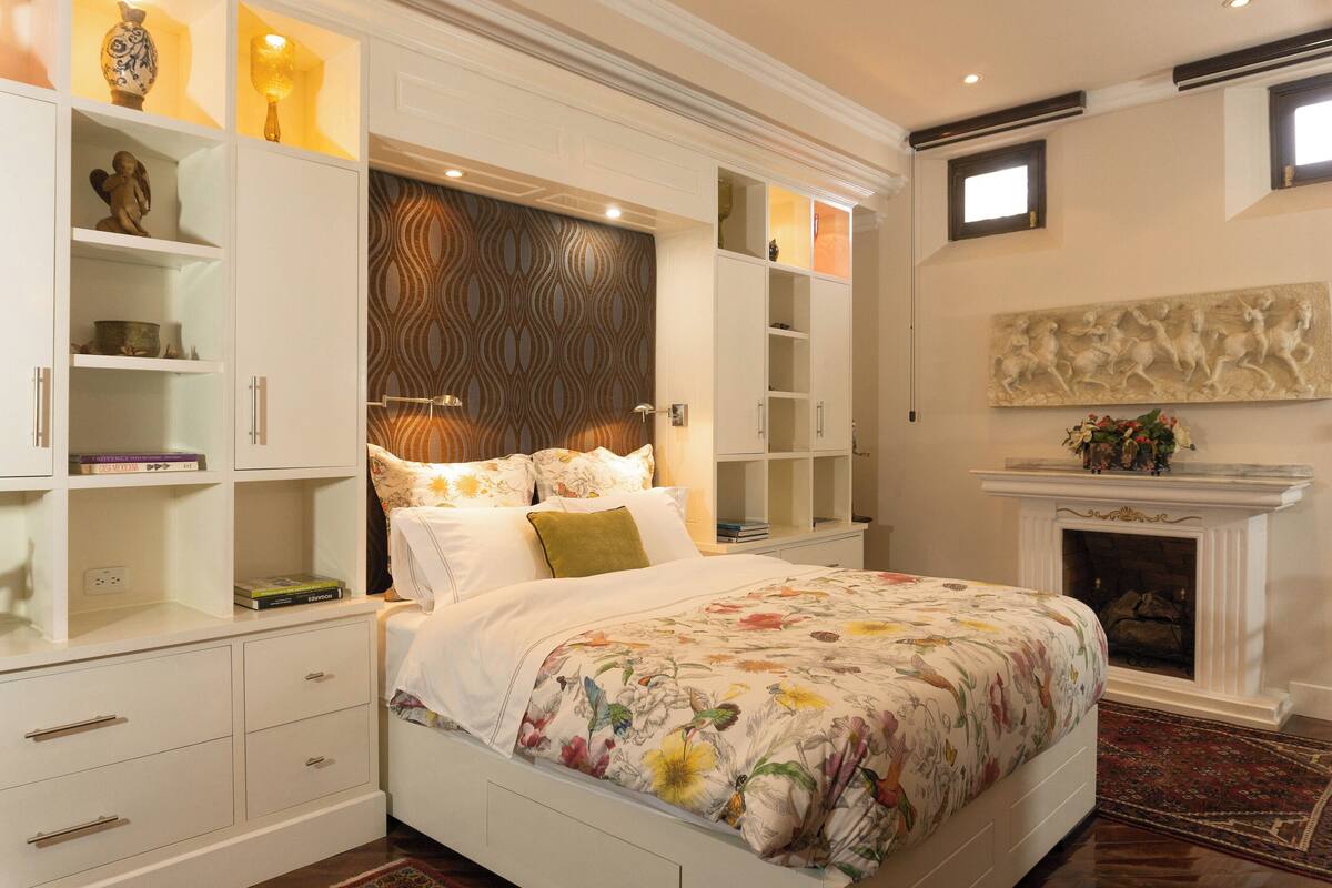 A bedroom with a large bed, built-in shelving, a fireplace, and a decorative wall piece.