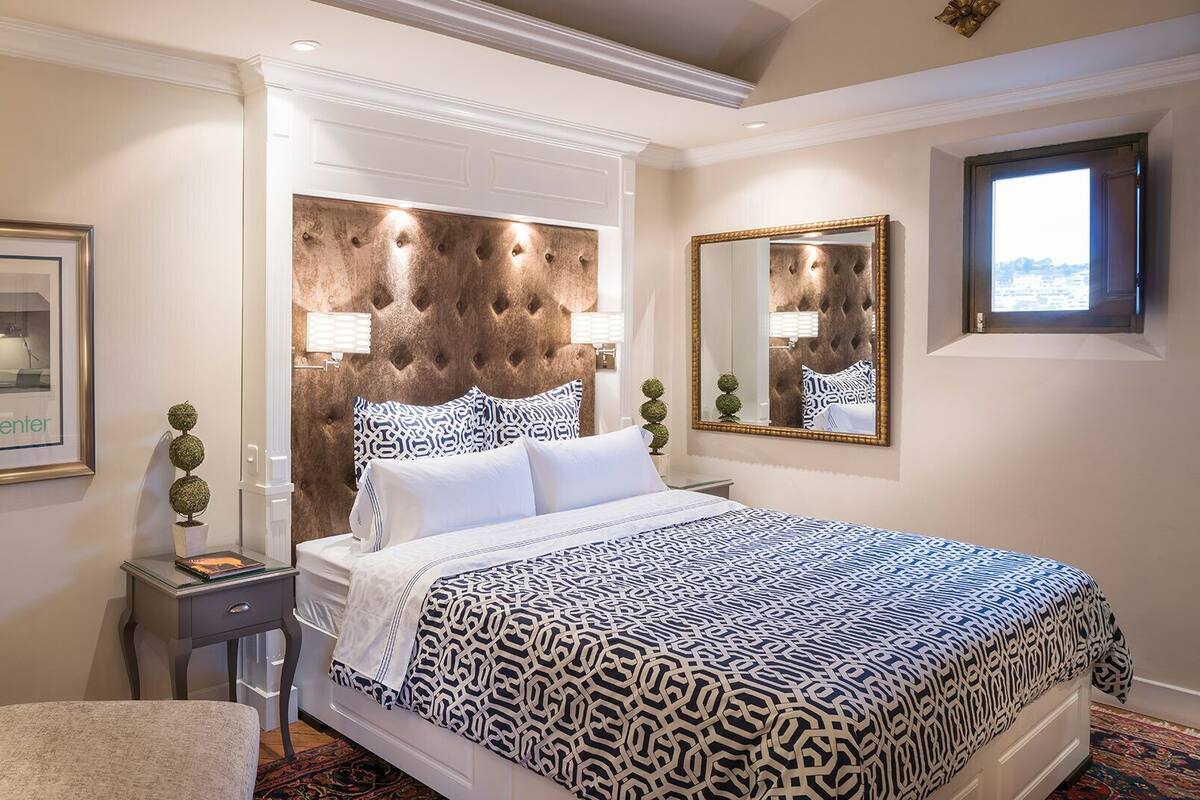 A hotel room with a large bed, a nightstand, a chair, a framed picture, and a mirror.