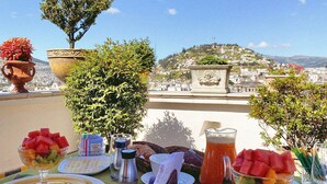 A table set with plates, cutlery, and a fruit bowl, overlooking a scenic view with hills and a church. - Villa Colonna (Quito)
