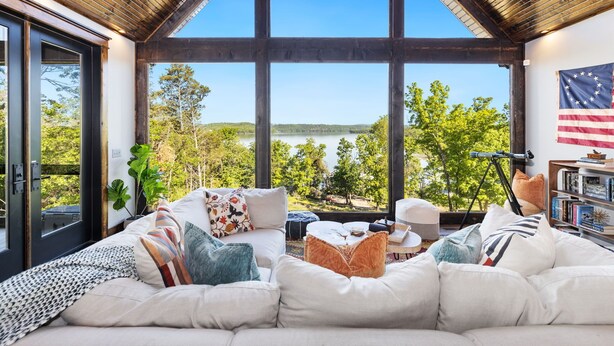 Ein geräumiges Wohnzimmer mit einem großen Fenster und Blick auf einen See und Bäume.