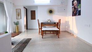 A dining area with a table and chairs, a decorative clock, and a painting on the wall. - Entire 2 BHK Suite With Kitchen (Mumbai)