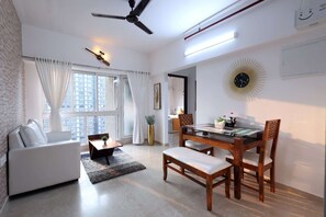 A modern living room with a sofa, a dining table with chairs, a ceiling fan, and a large window with curtains.