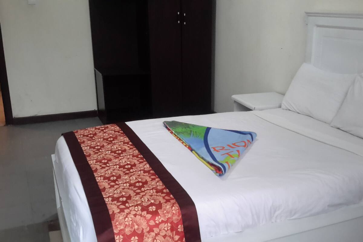 A neatly made bed with a floral-patterned bedspread and a colorful pillow.