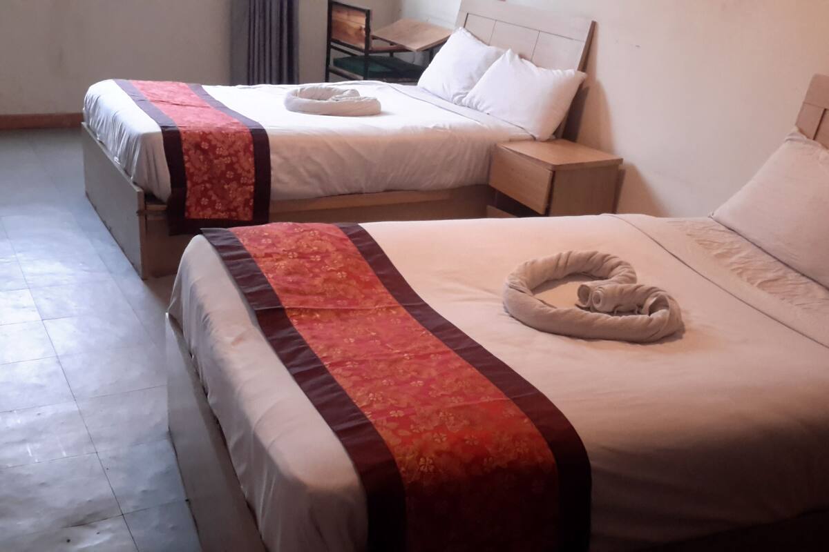 Two single beds with white linens and red floral bedspreads, each with a towel shaped like a heart.