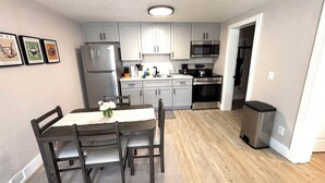 A compact kitchen with grey cabinets, a stainless steel refrigerator, a microwave, and a stove. There is a dining table with chairs and a vase of flowers. - Charming  1 bedroom apartment with AC, WiFi in quaint Columbus (Columbus)