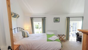 A bedroom with a bed, a wooden dresser, a radiator, a window with curtains, and a door. - Great Hartbarrow Farm Cottage (Windermere)