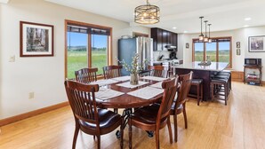 Een ruime keuken met een groot eiland, een houten eettafel met stoelen en uitzicht op een grasveld door grote ramen.