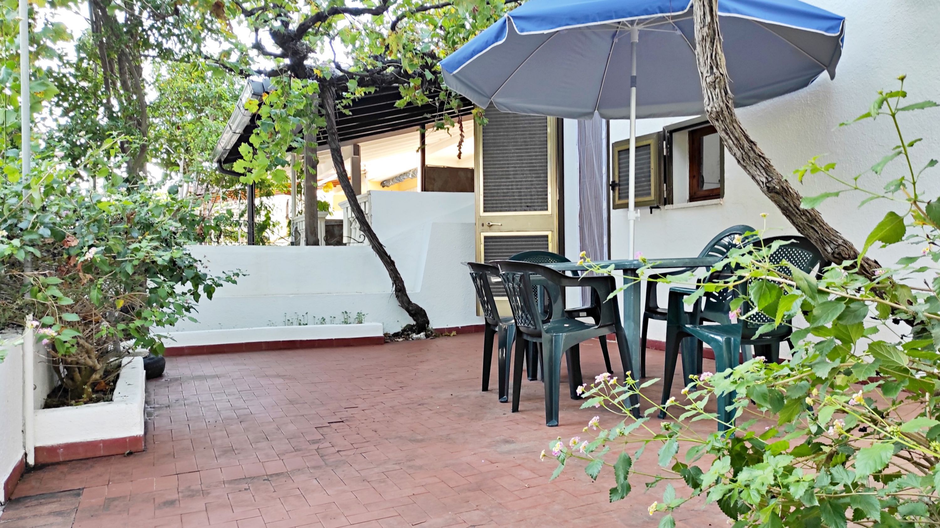A patio with a table and chairs, a hanging umbrella, and a white wall with a window.