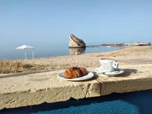 A beach scene with a pastry and a cup of coffee on a concrete ledge. - Casa Preula - A due Passi Dalla Spiaggia di Torre Pali (Salve)