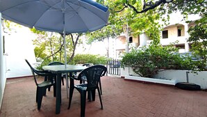 Un patio al aire libre con una mesa redonda y sillas, una sombrilla azul, y piso de ladrillo.