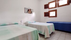 Una habitación con dos camas, una mesita de noche con lámpara, un espejo en la pared y dos ventanas.