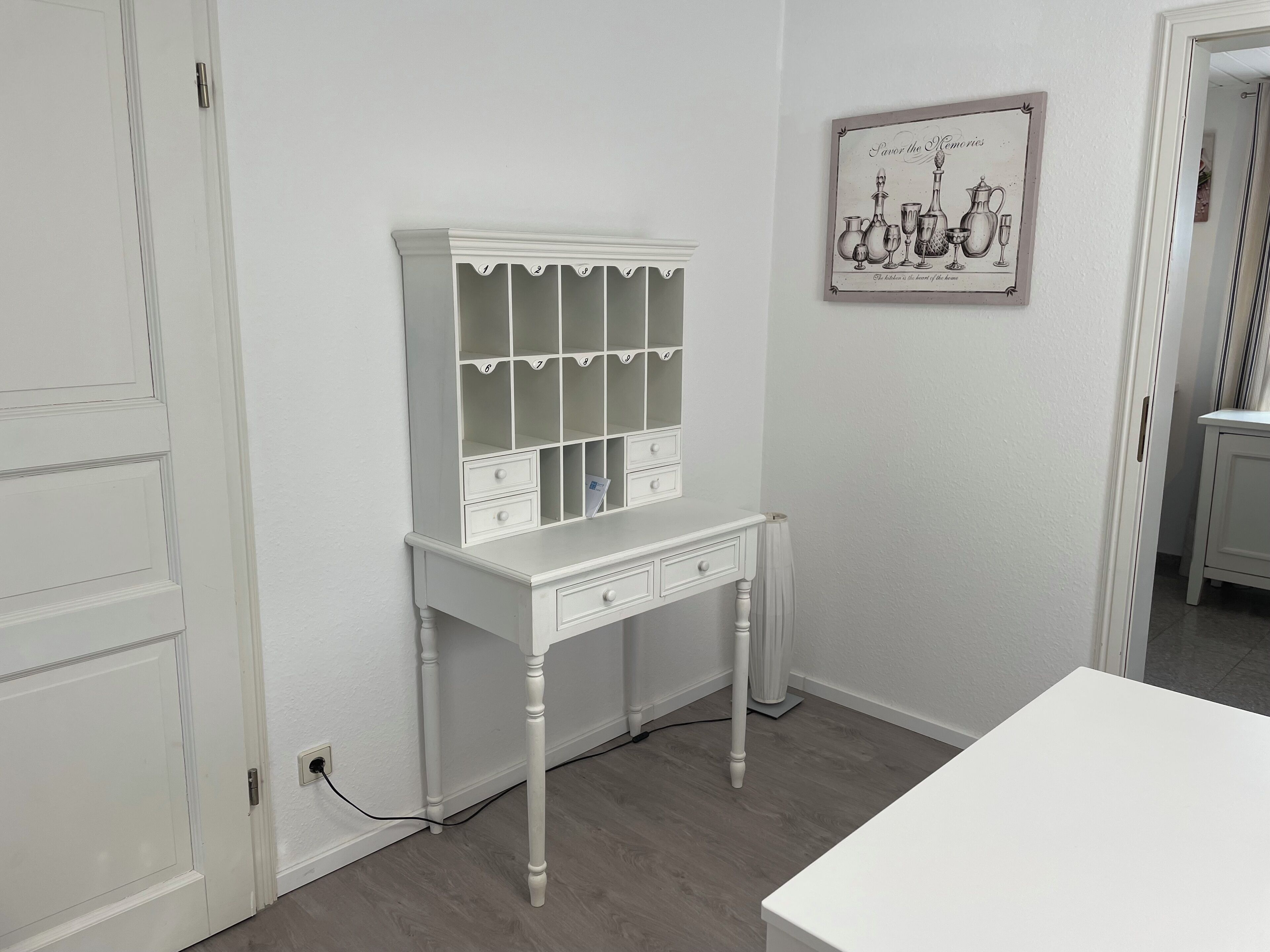 A white room with a white console table, a white cabinet with multiple drawers, and a framed picture on the wall.