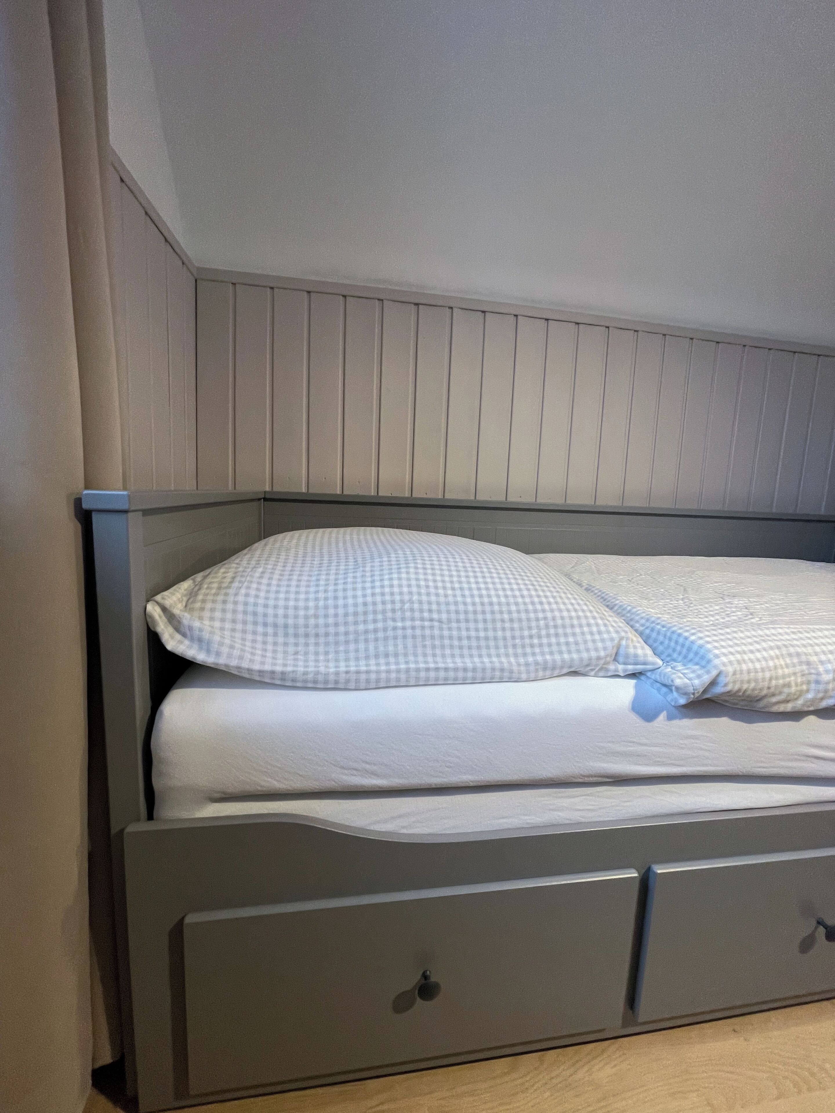 Un lit avec un oreiller à carreaux et une tête de lit grise.