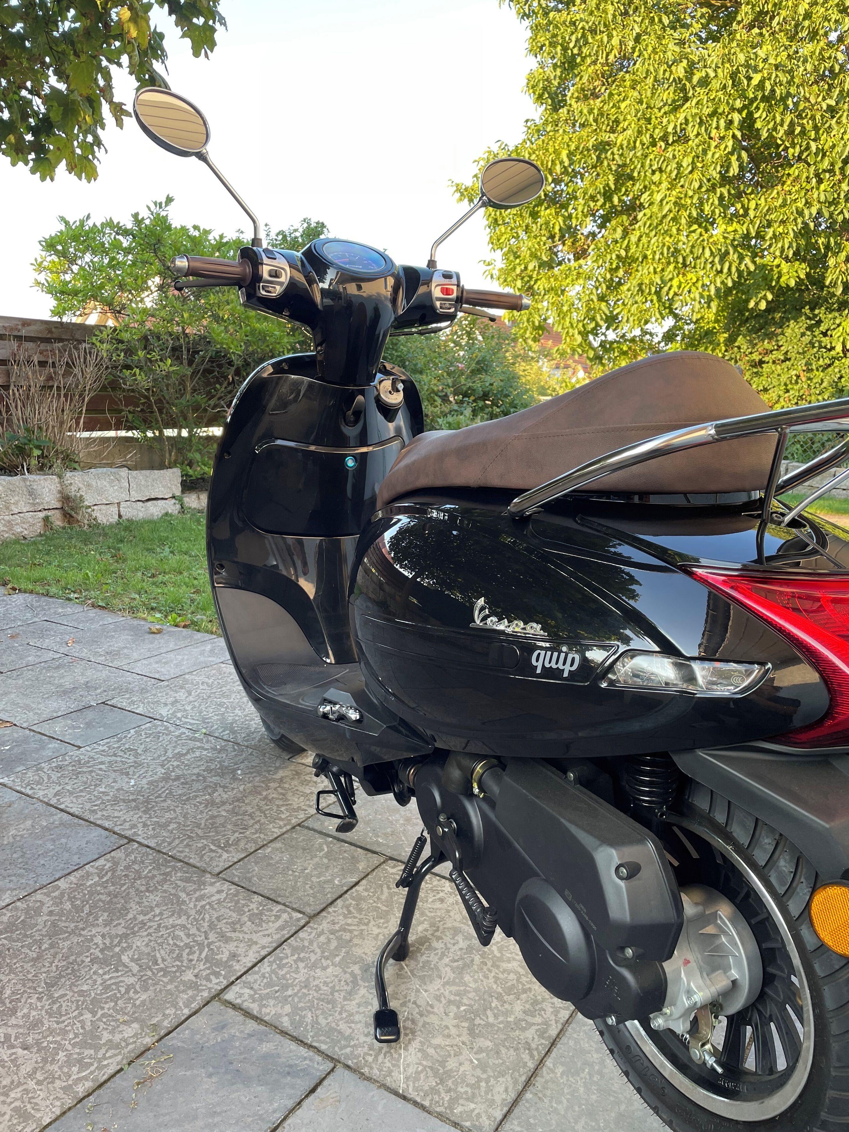 Uma scooter preta com assento marrom estacionada em uma superfície pavimentada.
