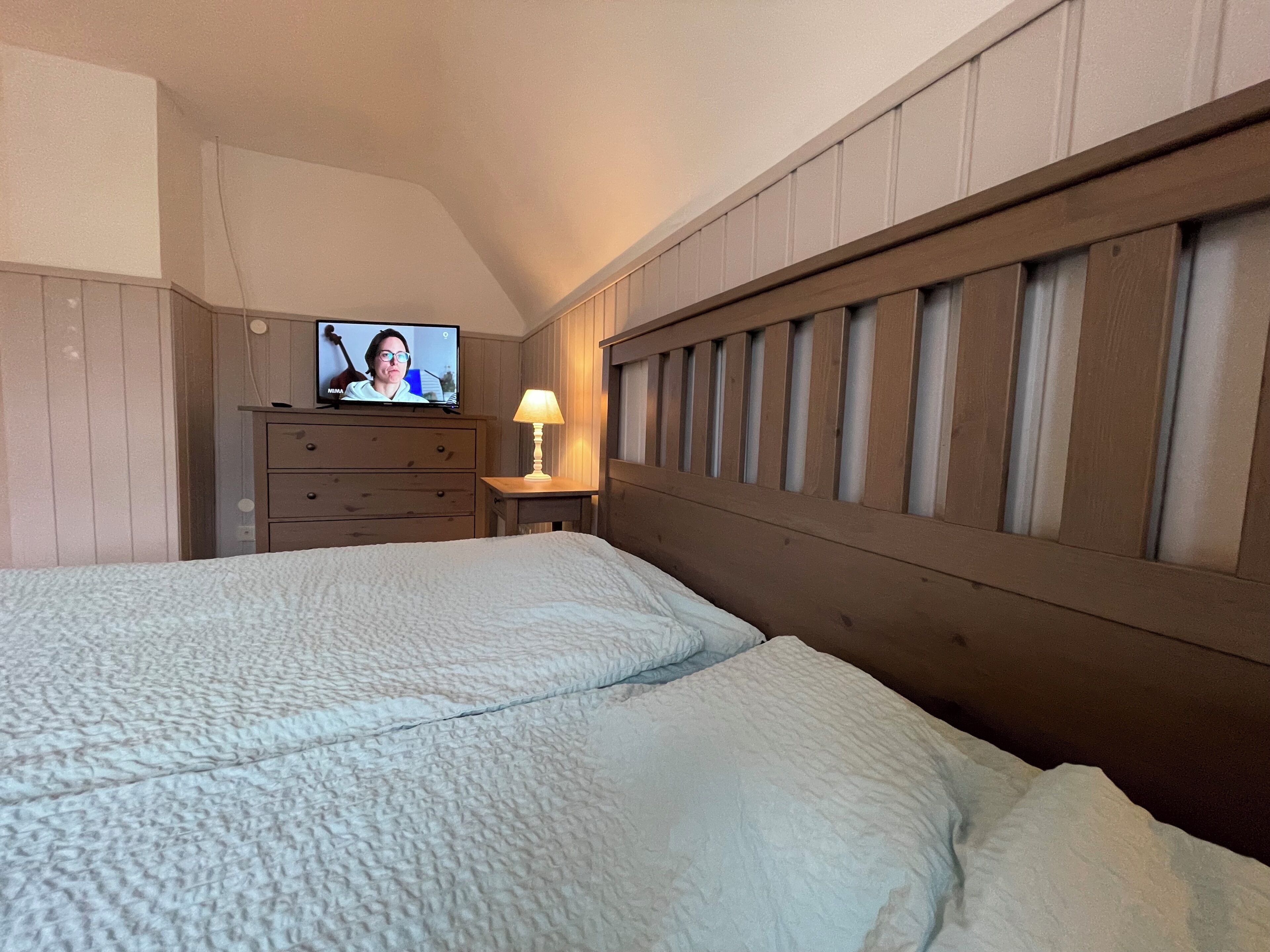 Ein Schlafzimmer mit zwei Betten, einem Fernseher auf einer Kommode und einer Lampe auf einem Nachttisch.