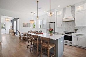 A modern kitchen with white cabinets, a central island with bar stools, a built-in oven, and pendant lighting.