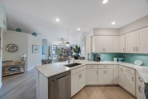 A modern kitchen with white cabinetry, a built-in dishwasher, and a teal backsplash.