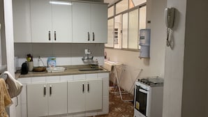 Una cocina compacta con gabinetes blancos, un lavamanos, un dispensador de agua y una estufa.