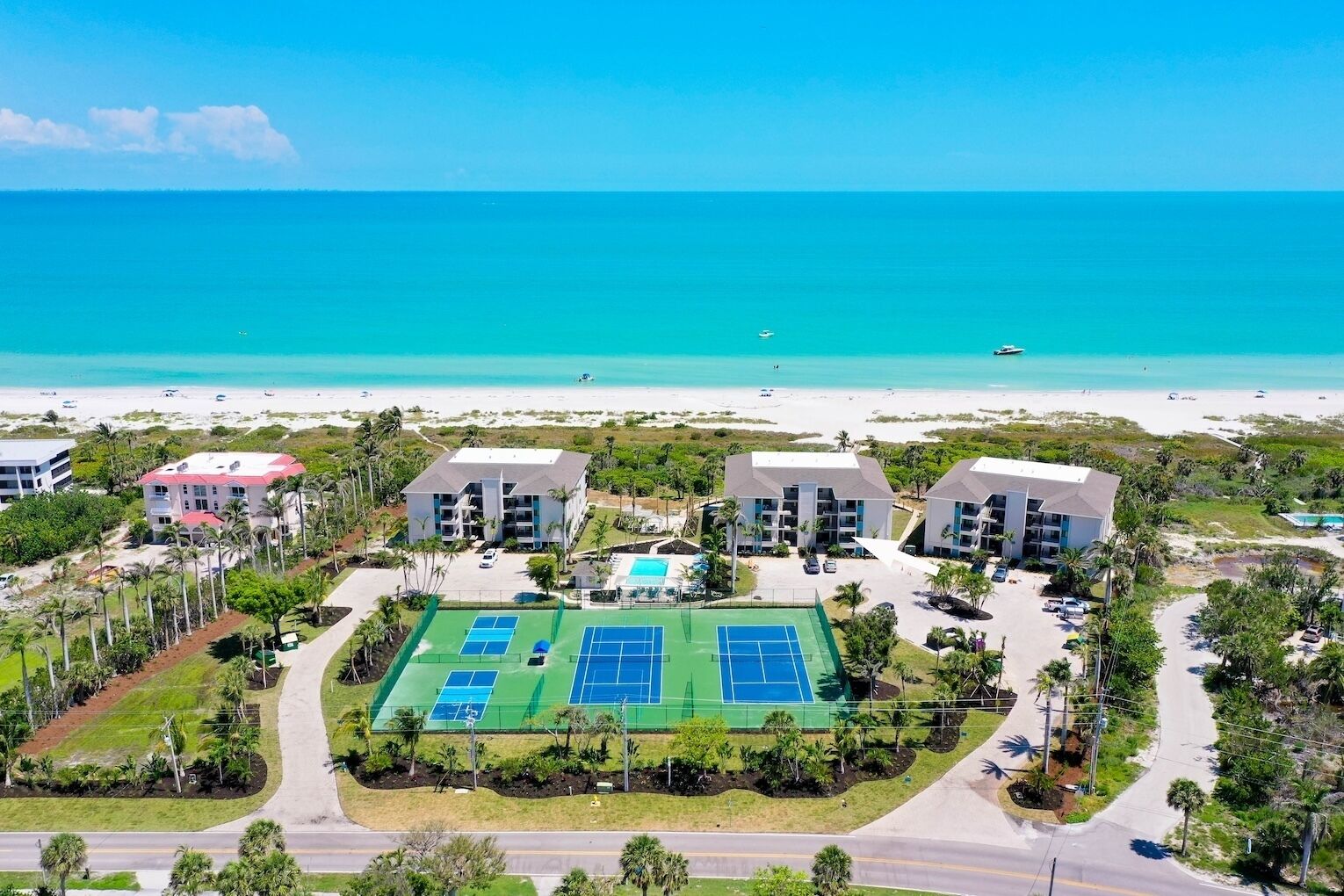 A resort with multiple buildings, a tennis court, and a beach view.
