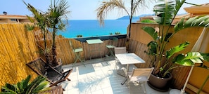 A patio with a table and chairs, a bamboo fence, and a view of the sea.