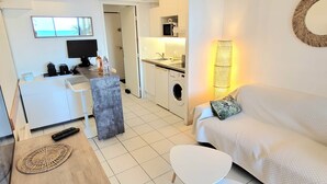 A modern living space with a sofa, a small white table, a coffee table, a TV, a kitchen area, and a washing machine. - "Theo'z Roof Top & Sea View" (Cannes)