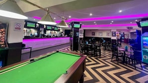 Una mesa de billar, una zona de bar con mostrador, y varias mesas y sillas en una sala con piso de diseño en zigzag.
