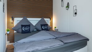 Een moderne slaapkamer met een bed, twee kussens, een nachtkastje met een plant en een wandlamp.