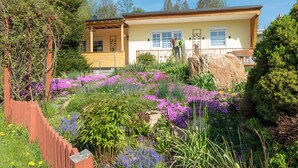 Een huis met een tuin ervoor, een houten omheining en een grote rots.