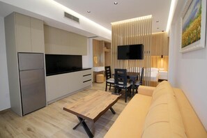 A modern kitchen with a built-in oven, a dining area with a wooden table and chairs, and a sofa. - Alis Apartments (Sarande)