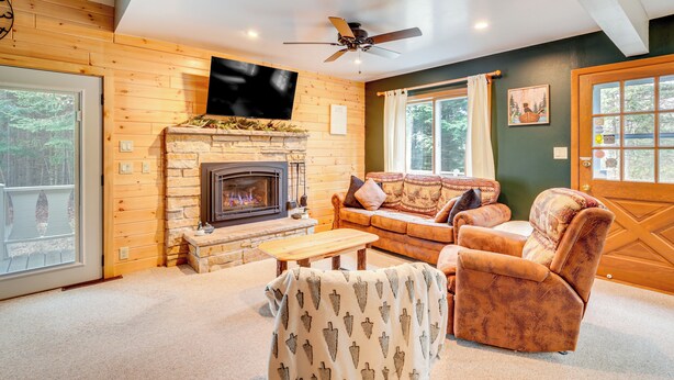A cozy living room with a fireplace, a sofa, a chair, and a television mounted on the wall. - Boat, Paddle, UTV & More: Getaway in Saint Germain (St Germain)