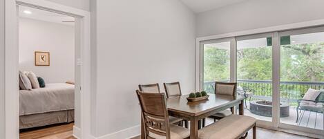 Un comedor con mesa y sillas de madera, un banco y vistas a un balcón con mobiliario exterior.