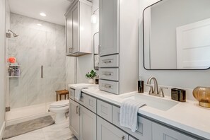 Ein modernes Badezimmer mit begehbarer Dusche, Toilette und Waschtisch inklusive Spüle und Spiegel.