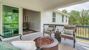 Eine überdachte Terrasse mit Gartenmöbeln, einer Feuerstelle und Blick auf ein Haus mit einer Terrasse.