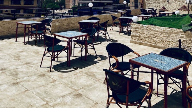 A rooftop terrace with tables and chairs, a view of the pyramid, and buildings in the background. - red pyramids hotel (Giza Governorate)