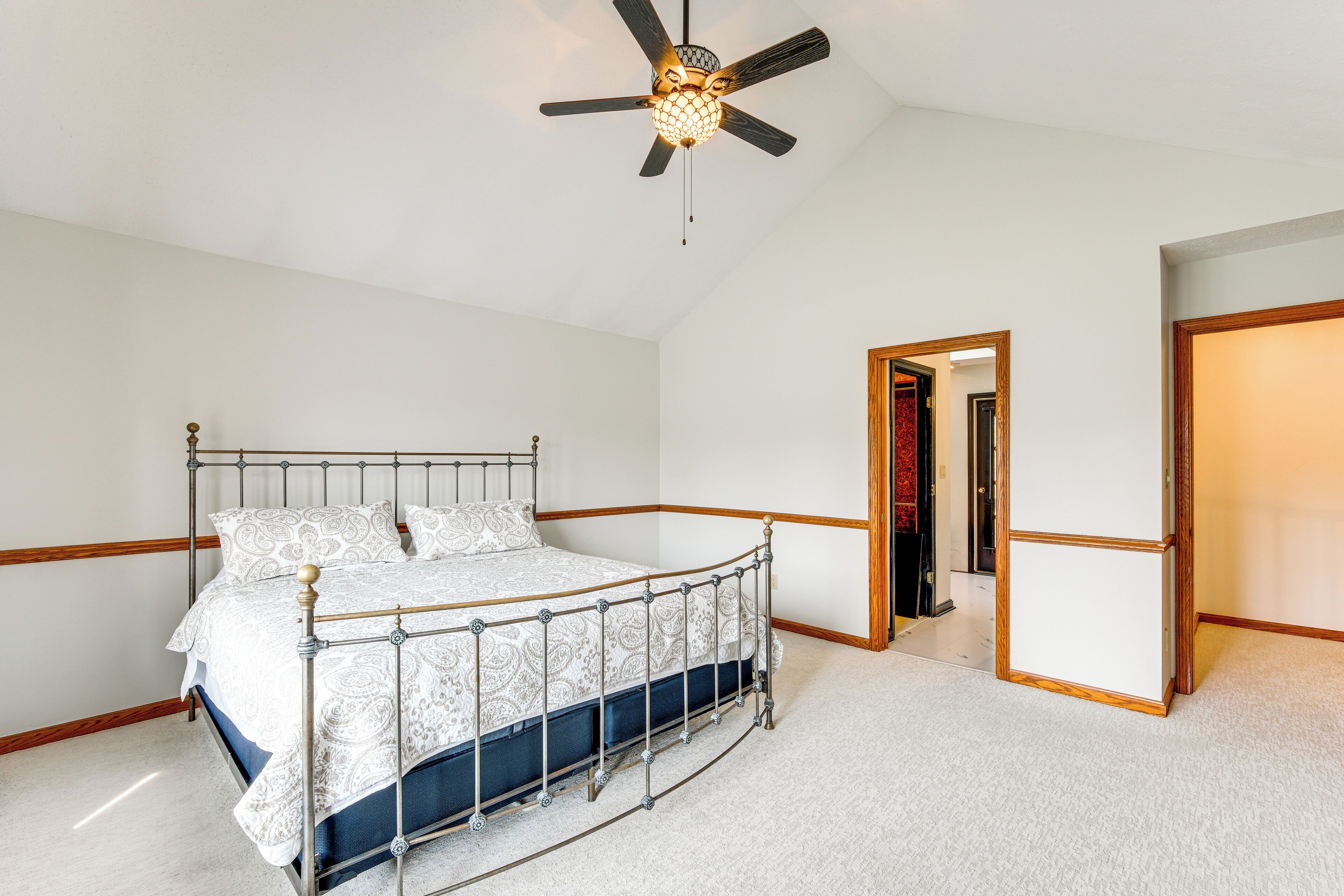 Une chambre à coucher avec un lit en métal, une literie blanche à motifs, un ventilateur de plafond et un sol recouvert de moquette.