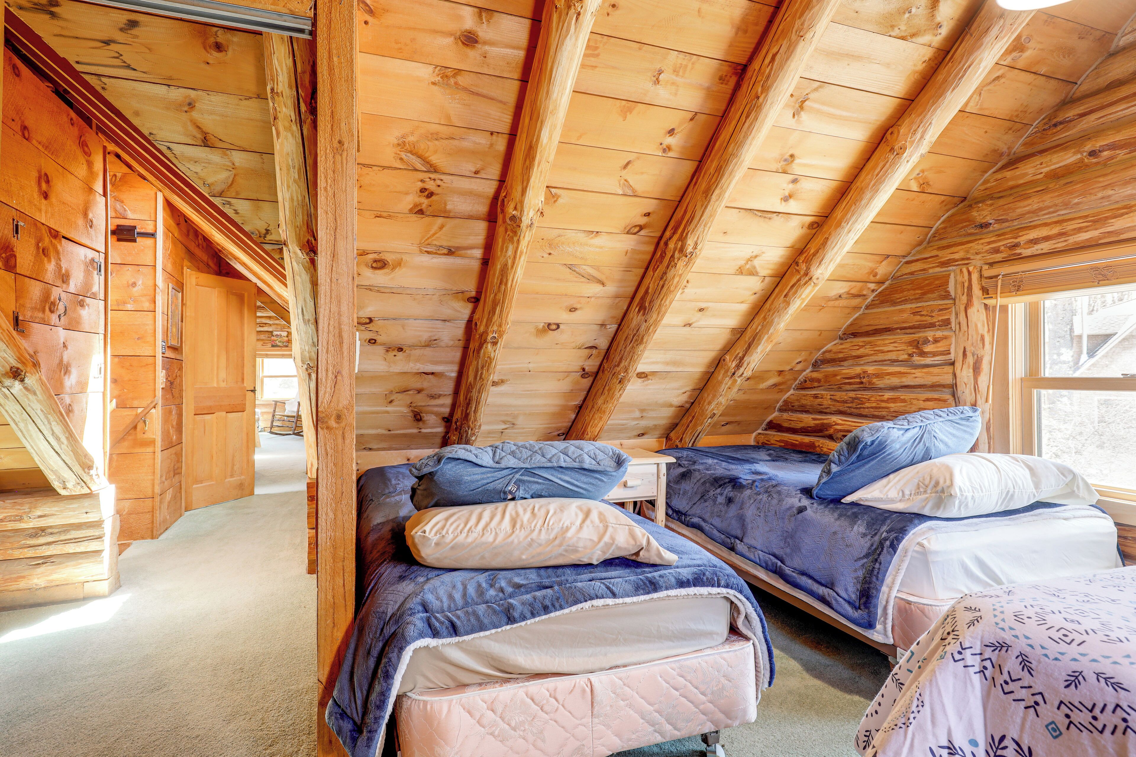 Une chambre mansardée en bois avec deux lits, une fenêtre et un escalier.