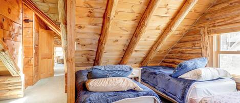 Une chambre mansardée en bois avec deux lits, une fenêtre et un escalier.