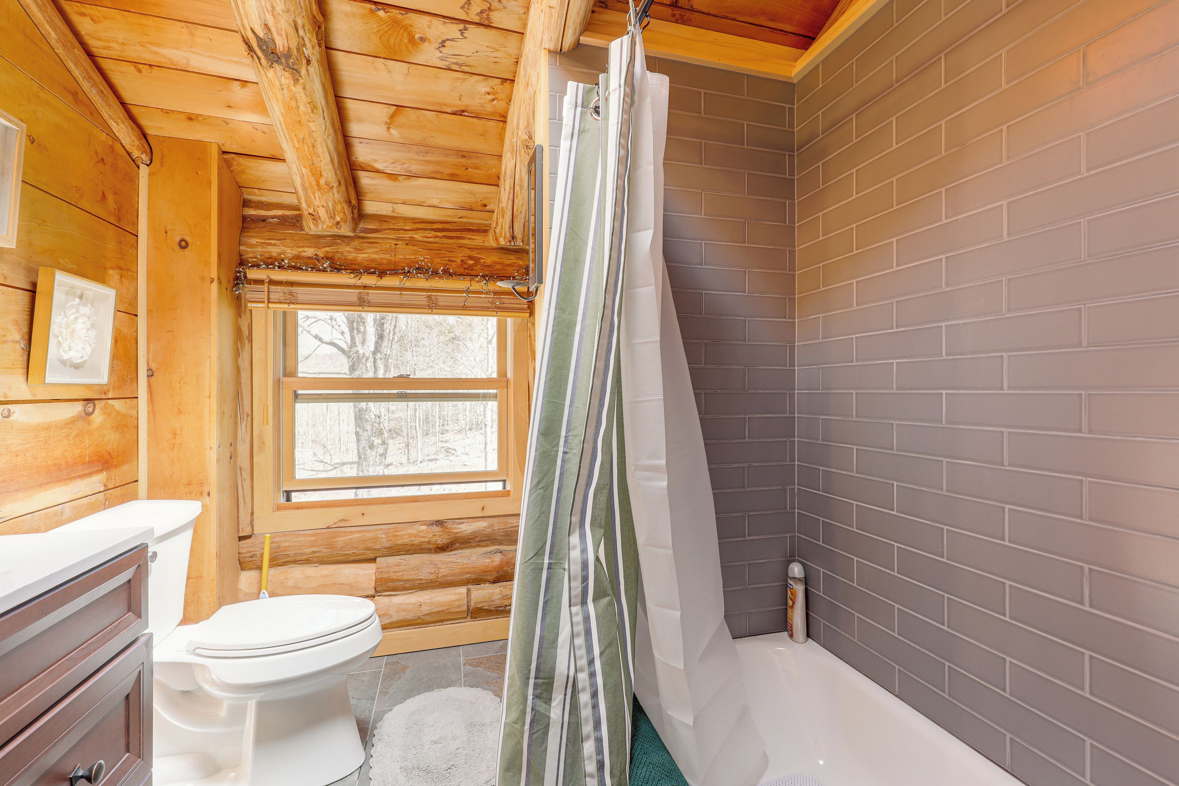 Baño de cabaña de madera con inodoro, ducha y ventana.