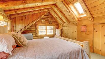 A cozy attic bedroom with a large bed, wooden walls, and a skylight.