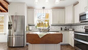 Una cuina moderna amb armaris blancs, un refrigerador d'acer inoxidable, una illa de fusta i un forn encastrat.
