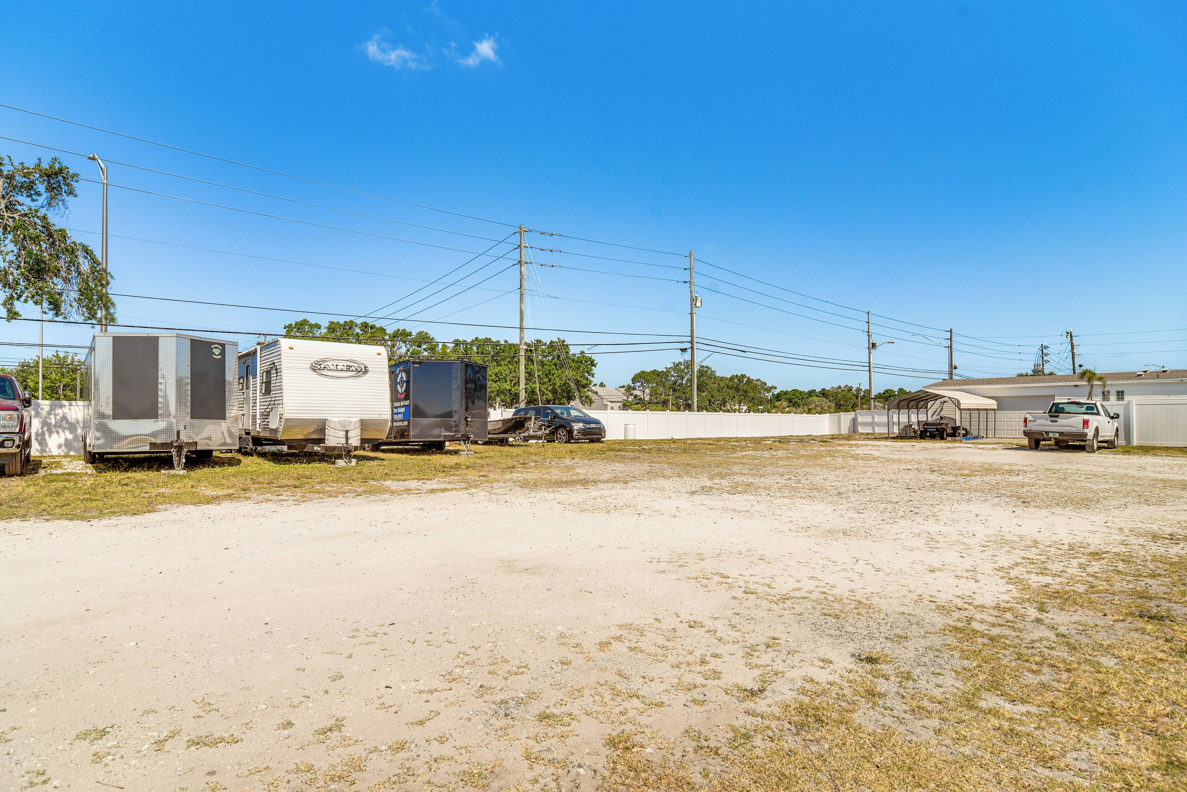 A parking lot with several RVs and trailers, a white fence, and utility poles.
